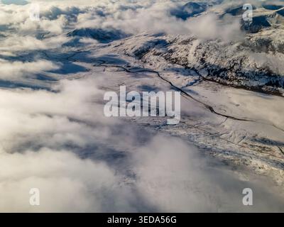 Aus der Vogelperspektive auf den schneebedeckten Babusar Pass mit einer gewundenen Straße durch Berggipfel und dicke weiße Wolken in Babusar, KPK, Pakistan. Stockfoto