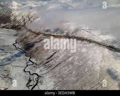 Aus der Vogelperspektive des Babusar Pass, der sich durch schneebedeckte Berghänge mit einem Fluss im Tal unter einem bewölkten Himmel schlängelt Babusar, KPK, Pakistan. Stockfoto