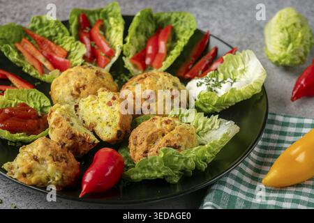 Ein Teller mit gebackenen Bällchen, Pizzabällchen umgeben von Salatblättern, Pfefferstreifen und Dip Stockfoto