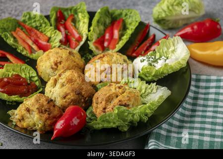 Ein Teller mit gebackenen Bällchen, Pizzabällchen umgeben von Salatblättern, Pfefferstreifen und Dip Stockfoto