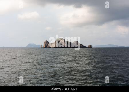 Blick von einer Fähre nach Koh Tao. Eine kleine felsige Insel steht im dunklen Meer. Ein bedeckter grauer Himmel hängt über dem Wasser. Stockfoto