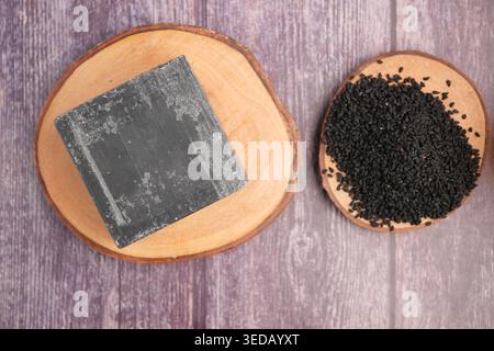 Schwarzkümmelsamen und Kräuterseife auf natürlichen Holzplatten Stockfoto