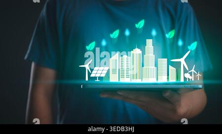 Mann mit Tablette mit grünem Eco City Hologramm. Nachhaltige Energie, ESG-Umweltkonzept, Solar- und Windenergietechnologie für die Zukunft Smart Urban l Stockfoto