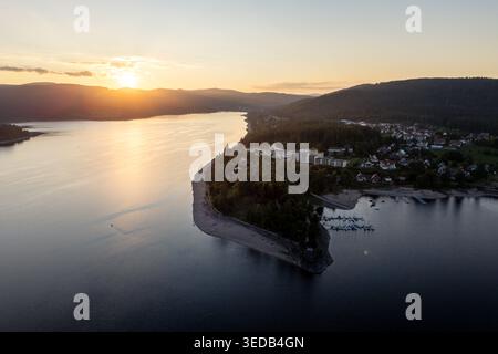 Blick aus der Vogelperspektive auf den Schluchsee bei Sonnenuntergang mit goldenem Licht, das auf dem Wasser reflektiert, bewaldete Hügel und das am See gelegene Dorf Schluchsee, Baden-Wurttem Stockfoto
