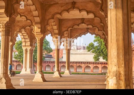 Verzierte Sandsteinbögen und Säulen der Mughal-Architektur im Agra Fort in Indien. Das Bild zeigt einen überdachten Gang mit aufwendig geschnitzten Stockfoto