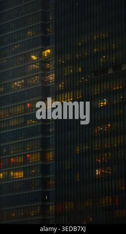 Moderne Bürotürme aus Glas, die nachts beleuchtet sind, mit leuchtenden Fenstern in Gelb-, Orange- und Rottönen. Stockfoto