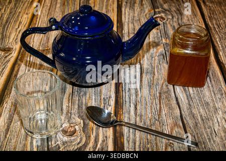 Hoher Winkel der Teekanne mit Deckel und Glas mit Honig auf Holztisch zusammen mit leerem Glas mit Löffel bei Tageslicht Stockfoto