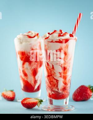 Erdbeermilkshake mit Schlagsahne und Beerensirup im hohen Glas auf blauem Hintergrund. Stockfoto