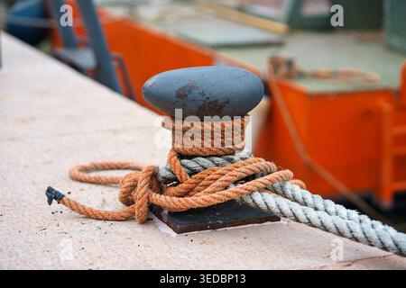 Nahaufnahme von Festmacherseilen, die um Metallpfoller auf dem Bootsdeck gebunden sind, nautische Details mit verschwommenem Yachthafen-Hintergrund, Seeverkehrskonzept Stockfoto