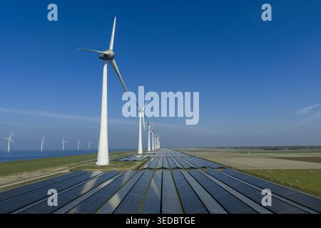 Luftaufnahme eines großen Solarparks und einer Reihe von Windturbinen entlang eines Küstendeichs unter klarem blauem Himmel Niederlande. Stockfoto