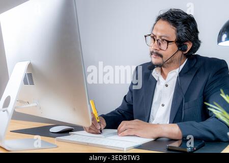 Ein professioneller junger männlicher Mitarbeiter nimmt mit einem Laptop an einer geschäftlichen Videokonferenz Teil, während er in einer modernen Büroumgebung arbeitet. Stockfoto