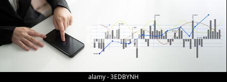 Ein Geschäftsmann interagiert mit einem Smartphone, das Finanzdaten anzeigt, während er Börsentrends auf einem nahegelegenen Bildschirm analysiert und moderne Geschäftsmodelle präsentiert Stockfoto