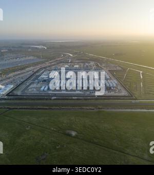 Luftaufnahme eines modernen KI-Rechenzentrums mit Kühlsystemen auf dem Dach, umgeben von grünen Feldern und einer flachen Landschaft unter einem weichen Sonnenuntergangshimmel Stockfoto