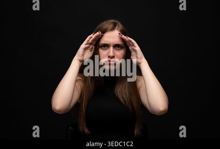 Frau fühlt sich gestresst, hat Kopfschmerzen und zeigt Anzeichen von Frustration und emotionaler Verärgerung auf schwarzem Hintergrund Stockfoto