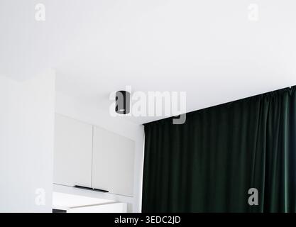 Moderne, minimalistische Inneneinrichtung mit schwarzer Deckenleuchte und dunkelgrünen Samtvorhängen, die eine klare weiße Wand betonen Stockfoto