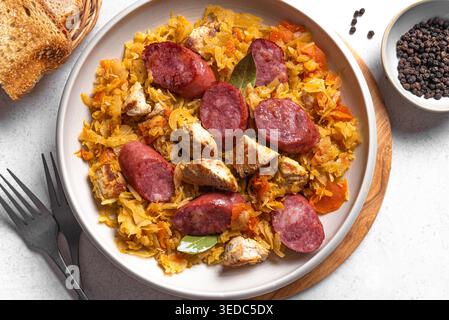 Traditionelle polnische Bigos-Mahlzeit oder Hunter's Stew mit Würstchen, Fleisch und gedünstetem Kohl in Keramikschale, Blick von oben. Hausgemachtes geschmortes Sauerkraut mit Bratwurst. Stockfoto