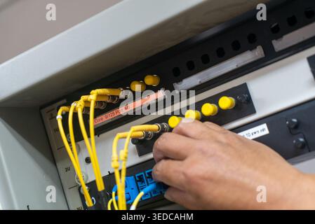 Eine Nahaufnahme der Hand eines Technikers, die Netzwerkkabel in einem Serverraum verbindet, zeigt moderne Technologie und Datenverwaltungsgeräte. Stockfoto