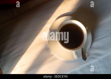 Ein ruhiges Bild mit einer Kaffeetasse auf einem Kissen, beleuchtet von sanftem Sonnenlicht. Diese friedliche Szene fängt das Wesen des morgendlichen Komforts ein Stockfoto