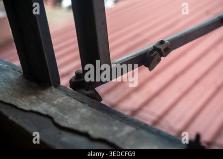Eine detaillierte Nahansicht eines Fensterrahmens mit Metallverriegelungen und -Strukturen. Die Aufnahme fängt ein kontrastierendes rotes Dach außen ein und bietet ein rustikales C Stockfoto