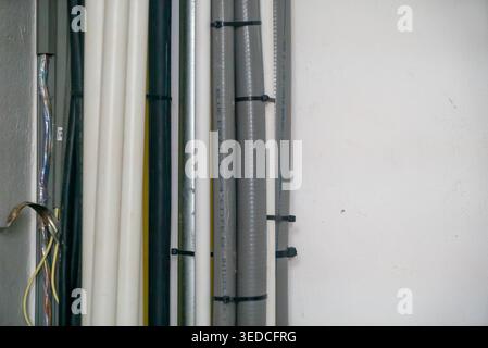 Eine übersichtliche Anordnung verschiedener Rohre und Kabel, die an einer Wand befestigt sind, bietet eine effiziente Einrichtung für Versorgungs- und Wartungsaufgaben in einer Lagerumgebung. Stockfoto
