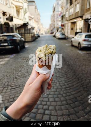 Pistazien-Eiskegel in der Hand auf einer kopfsteingepflasterten Straße in Belgrad. Urbanes Sommer-Snackkonzept für Reisen, Tourismus, lokale Küche und Stockfoto
