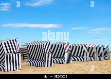 Eine Reihe traditioneller gestreifter Liegestühle aus den Windstrandkörben an einem Sandstrand an der Ostseeküste. Stockfoto