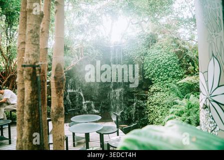 Eine ruhige Gartenszene mit einem ruhigen Wasserfall umgeben von üppigem Grün und eleganten Sitzgelegenheiten, perfekt zum Entspannen und Entspannen in die Natur. Stockfoto