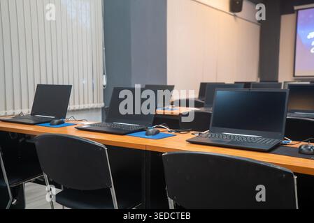Ein moderner Arbeitsbereich mit mehreren Laptops auf Holzschreibtischen und ergonomischen Stühlen. Ideal für Schulungen, Meetings oder pädagogische Zwecke Stockfoto