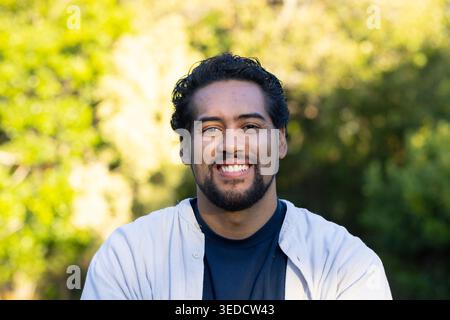 Afroamerikaner posiert und lächelt im Sonnenlicht des Parks, trägt ein helles Hemd über dunklem T-Stück Stockfoto