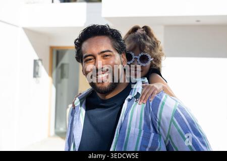 Afroamerikaner Vater trägt die Tochter in einem weißen Haus mit gestreiftem Hemd und Blumenschirmen Stockfoto
