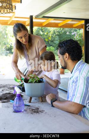 Verschiedene Familien, die Setzlinge auf überdachter Terrasse topfen, Frau, die aus grüner Dose gießt, Erde verschüttet Stockfoto