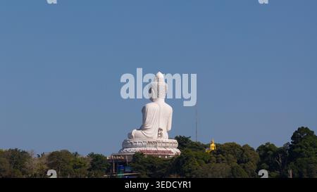 Aus der Vogelperspektive der Big Buddha Statue aus weißem Marmor, die auf einem üppig grünen Hügel unter einem klaren blauen Himmel in Tambon Karon, Chang Wat Phuket, Thailand, sitzt. Stockfoto