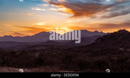 Dramatische Sonnenuntergangslandschaft mit Bergsilhouetten unter einem lebendigen Himmel mit warmen Farben, die eine natürliche und stimmungsvolle Abendszene einfangen. Stockfoto