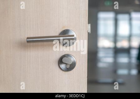 Nahaufnahme eines modernen Türgriffs, der an einer Holztür befestigt ist. Das elegante Metalldesign und die schlichte Ästhetik ergänzen die moderne Inneneinrichtung. Stockfoto