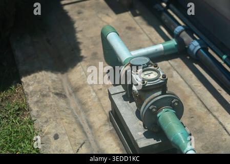 Nahaufnahme eines Wasserdurchflussmessers, der auf einem grünen Rohrsystem positioniert ist und wichtige Komponenten zeigt, die für die Messung des Wasserdurchflusses im Außenbereich verwendet werden. Stockfoto