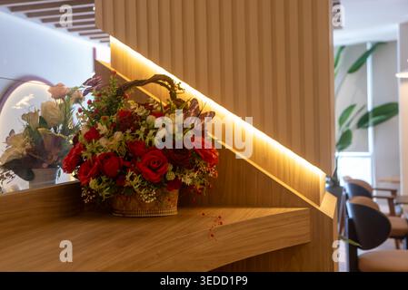 Ein atemberaubendes Blumenarrangement mit roten Rosen in einem gewebten Korb, elegant in einem modernen Innenraum platziert, schafft einen warmen und einladenden geldautomaten Stockfoto