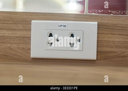 Nahaufnahme einer weißen Steckdose auf einer Holzoberfläche, die modernes Design und Funktionalität für den privaten oder gewerblichen Gebrauch zeigt Stockfoto