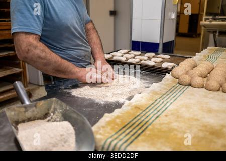 Baker Hands kneten Brotteig auf einer mit Mehl bedeckten Werkbank und bereiten ihn für das Backen in einer handwerklichen Bäckerei vor Stockfoto