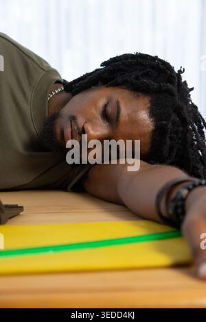 Afroamerikaner, der auf Holztisch ruht, mit gefaltetem Arm, olivem Tee, gelbem Notizbuch in der Nähe Stockfoto