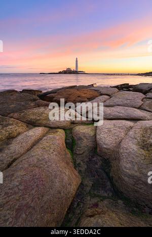 Farbenfroher rosafarbener Sonnenaufgang am St. Marys Lighthouse mit Felsen an der Küste. Whitley Bay, North Tyneside, England, Großbritannien. Stockfoto