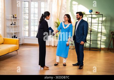 Eine indische Immobilienmaklerin oder Architektin und ein junges verheiratetes Paar schütteln sich die Hände in einem neuen Zuhause, um den Immobilienvertrag abzuschließen und ihren Erfolg zu feiern Stockfoto