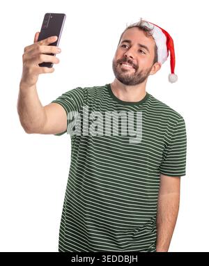 Ein bärtiger Mann lächelt lustig, als er sein Handy benutzt, um ein Selfie zu machen. Er trägt einen Weihnachtsmann-Hut, der zeigt, wie viel Spaß er an den Feiertagen hat. Stockfoto