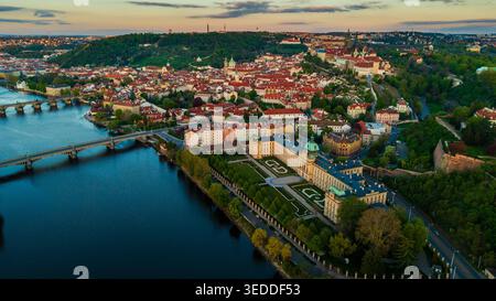 Aus der Vogelperspektive auf die Prager Burg, die Moldau und historische Gebäude mit roten Dächern unter einem warmen Sonnenuntergang Prag, Prag, Tschechien. Stockfoto