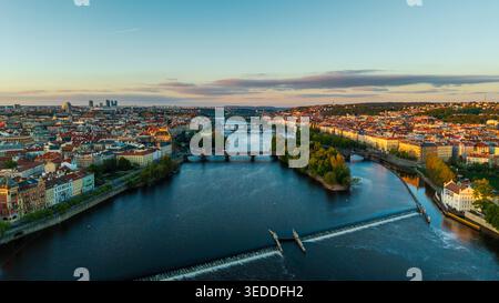 Blick aus der Vogelperspektive auf die Moldau, die durch das historische Stadtzentrum mit seinen berühmten Brücken und Gebäuden mit roten Dächern unter einem weichen Sonnenuntergang in P fließt Stockfoto