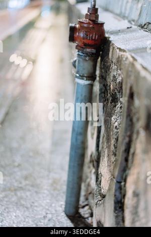 Nahaufnahme des verwitterten roten Hydranten, der an einer Betonwand neben dem Bürgersteig montiert ist, geringe Tiefe von Stockfoto