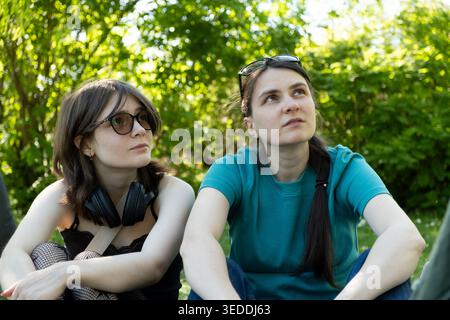 Zwei Schwestern unterschiedlichen Alters sitzen auf Gras und schauen nach oben. Stockfoto