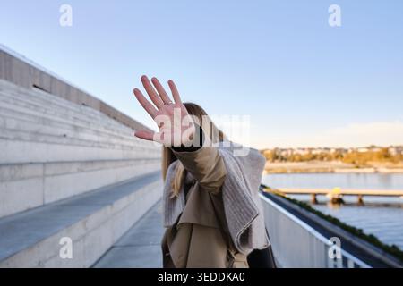 Frau im Grabenmantel bedeckt die Kamera mit ihrer Hand, die im Freien Stop Geste macht Stockfoto