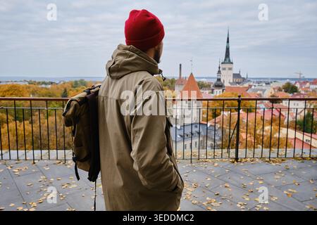 Mann mit Rucksack und roter Mütze, der im Herbst die historische Skyline von Tallinn betrachtet Stockfoto