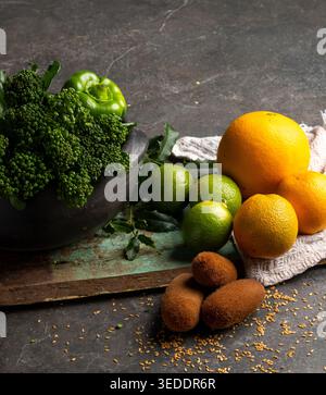 Brokkoli, grüne Paprika, Orangen, Limetten und andere Früchte werden mit einem Tuch darunter auf eine Holzoberfläche gelegt. Natürliches Licht liefert klare Details von Stockfoto