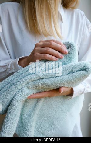 Frau in einem weißen Hemd, die drinnen einen Stapel weicher, sauberer, hellblauer Handtücher hält Stockfoto